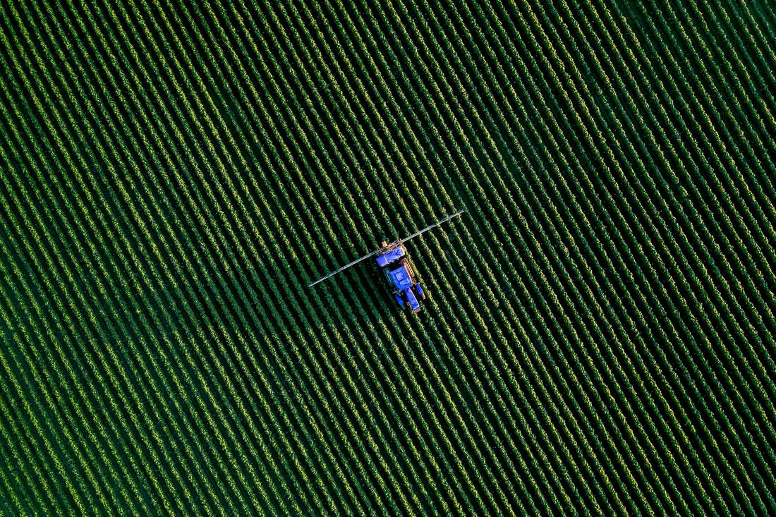 Vista aérea de un tractor pulverizador avanzando dentro del cultivo